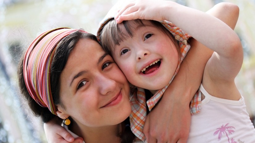 Special needs child smiling and holding/hugging her young female caregiver or relative